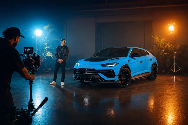 Baby-blue Lamborghini Urus Performante on an illuminated music-video set with a performer and camera crew