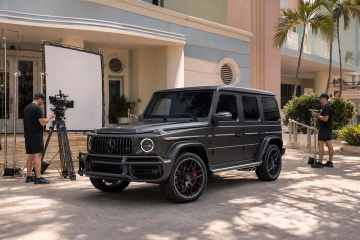 Matte-black Mercedes-AMG G 63 at an Art Deco film set with crew, a cinema camera and a diffusion panel